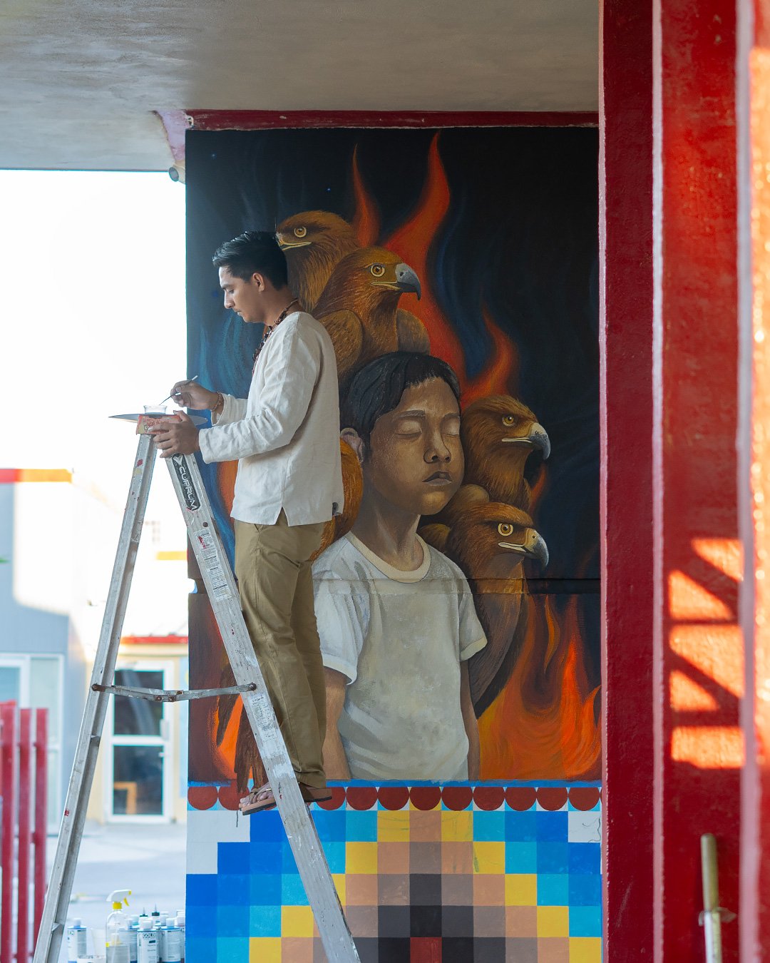 An artist on a ladder painting the school mural, a child’s face surrounded by eagles and flames