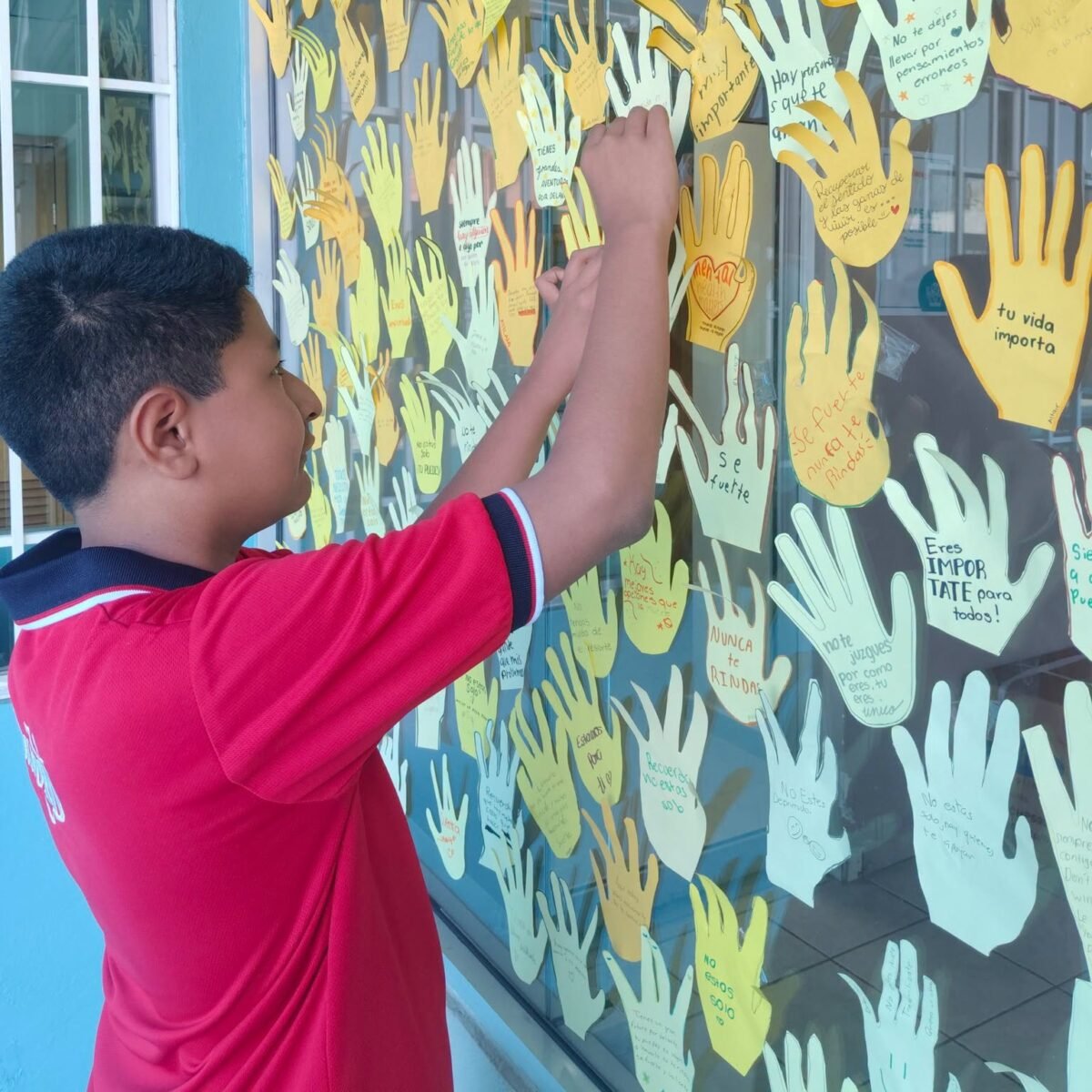 A student adds his paper hand to the window display of messages.