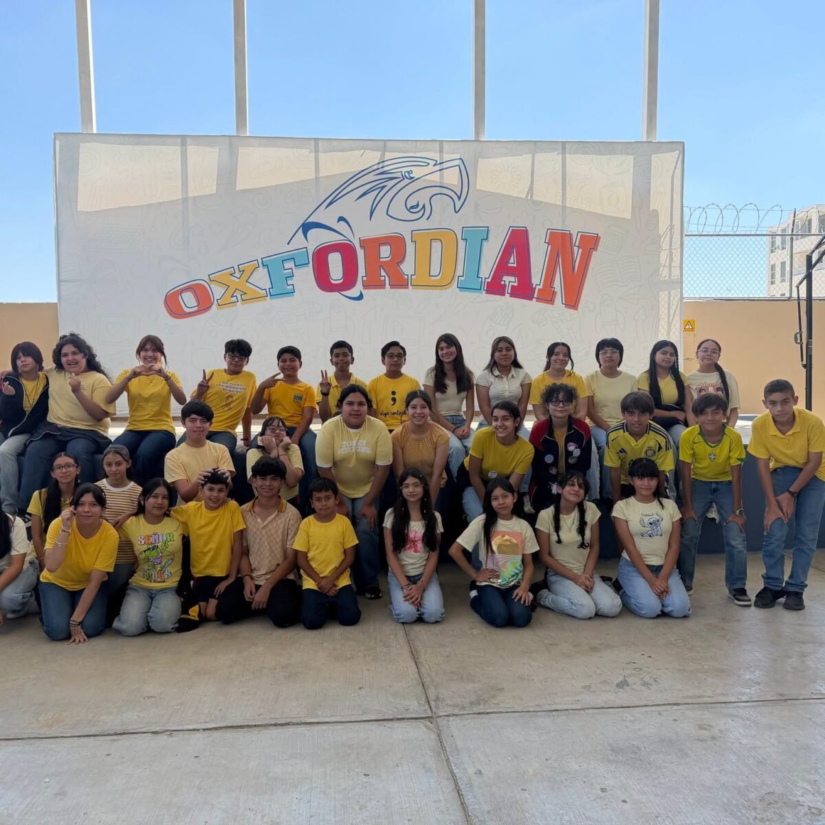 A group of students dressed in yellow in front of the Oxfordian banner.