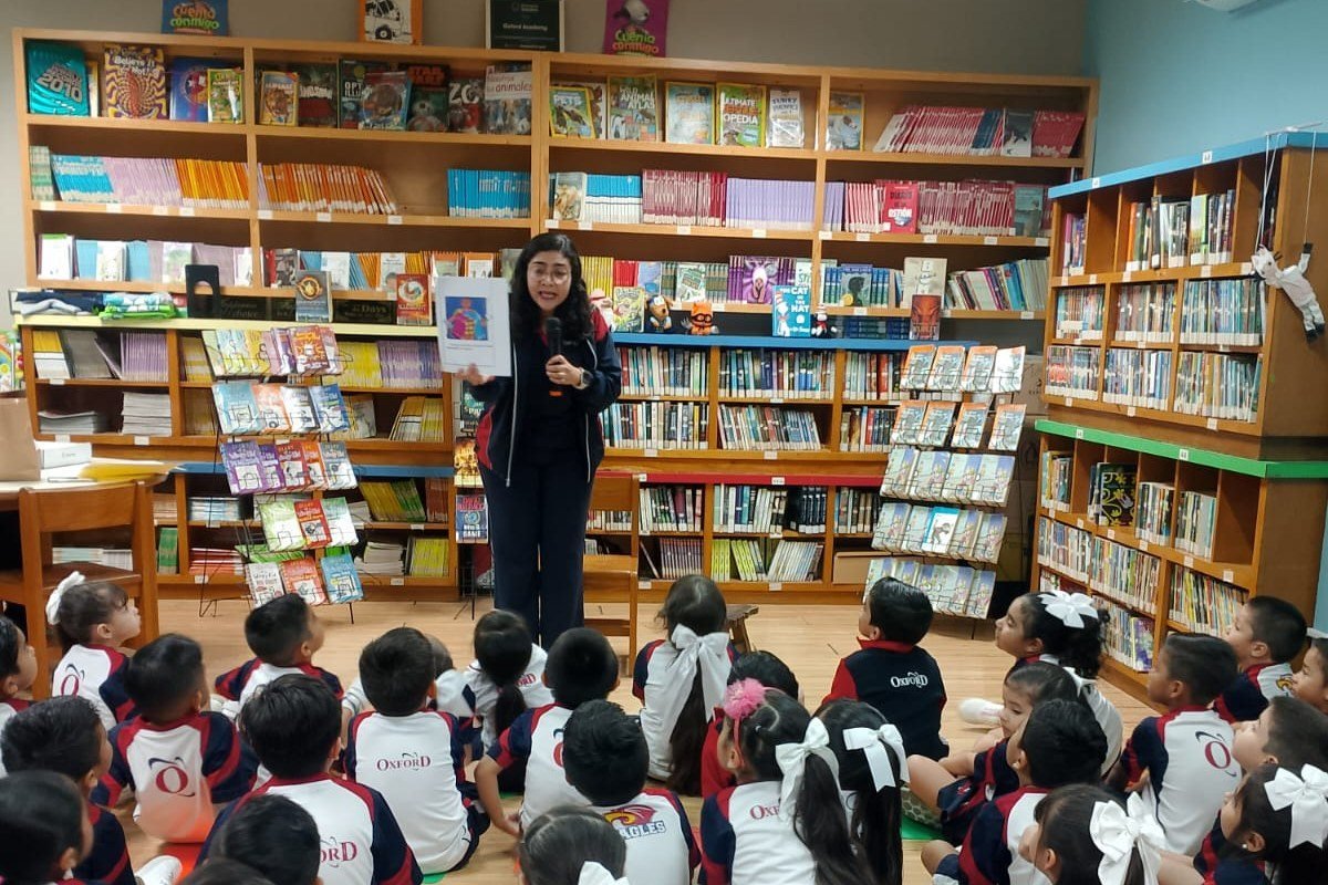 The librarian holding up a picture book while Kínder children sit on the library floor listening